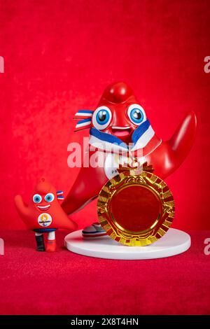 ZHONGSHAN Chine-22 mai 2024 : 2024 Paris Jeux Olympiques et Jeux Paralympiques mascottes les Phryges avec la médaille d'or sur fond rouge à composition verticale Banque D'Images