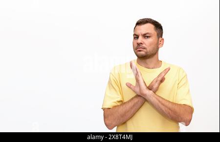 Personne masculine portant un t-shirt jaune se tient sur fond blanc et faisant un geste de refus, de restriction, de non, de refus, avec les mains croisées. Banque D'Images