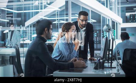Équipe de spécialistes de l'Agence de conception industrielle discutant d'un modèle de carte de circuit imprimé 3D créé sur un logiciel de CAO sur un ordinateur de bureau. Jeunes hommes et femmes travaillant dans Electronics Development Factory. Banque D'Images