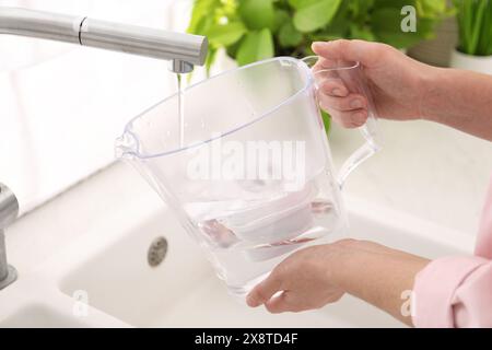 Femme remplissant le pichet filtrant avec de l'eau du robinet dans la cuisine, gros plan Banque D'Images