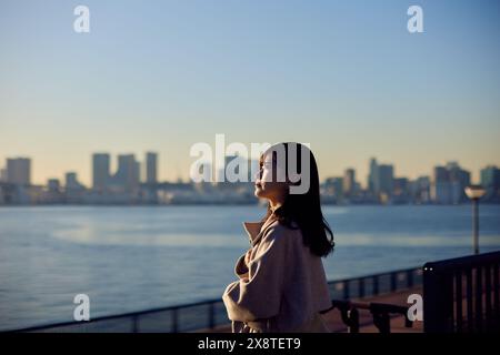 Femme japonaise debout près de l'eau regardant la ville Banque D'Images