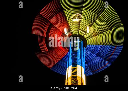 Lumières néon tricolores du carrousel tournant avec ciel sombre sur fond, effet d'exposition longue Banque D'Images