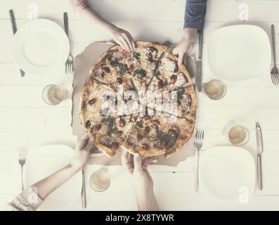 quatre mains prenant des morceaux de pizza vue de dessus, tonifié avec filtre instagram Banque D'Images