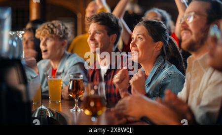 Groupe d'amis divers encourageant leur équipe, buvant de la bière dans un comptoir de pub. Fans de soutien acclamant, applaudissant et criant. Des amis joyeux célèbrent la victoire après le but. Banque D'Images