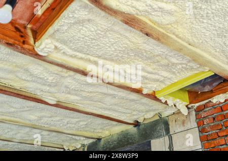 Isolation du plafond dans la maison avec de la mousse de polyuréthane. Mousse isolante entre poutres en bois Banque D'Images