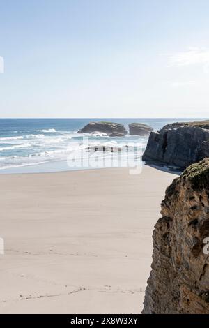 plage sereine avec falaises, vagues océaniques, ciel dégagé et une formation rocheuse isolée au large Banque D'Images