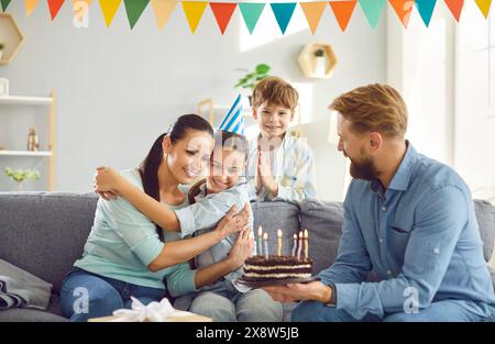 Grande famille heureuse célèbre l'anniversaire de la fille avec des bougies ornées de gâteau. Les desserts et décorations préférés de la fille pour l'anniversaire remplissent la pièce comme ils Banque D'Images