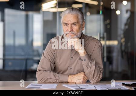 Homme d'affaires senior dans le bureau moderne, profondément axé sur les documents de travail, montrant l'expérience et le professionnalisme Banque D'Images