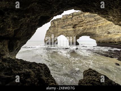 Un affleurement rocheux à Marinha Beach, Portugal, silhouette contre la douce lumière d'un ciel nuageux. Les vagues se jettent doucement sur le rivage, créant une côte sereine Banque D'Images