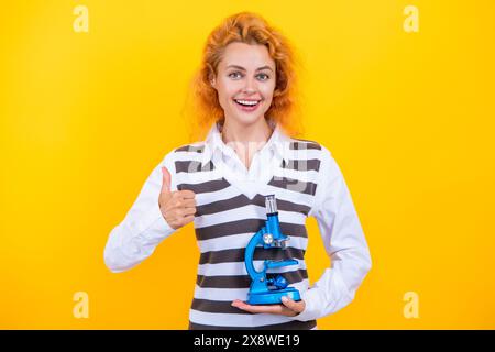 Une femme professeur de biologie scolaire tient un microscope. Femme professeur de biologie. Retour à l'école. Professeur avec microscope isolé sur jaune. Sciences biologiques Banque D'Images