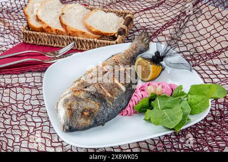 Dorade grillée sur assiette avec citron, salade et légumes grillés. Dorade de mer frite sur assiette avec un citron. Nourriture saine. Banque D'Images