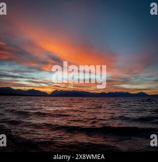Magnifique coucher de soleil sur une mer tranquille avec un ciel orange et bleu vibrant, des montagnes silhouettées contre l'horizon au loin Banque D'Images