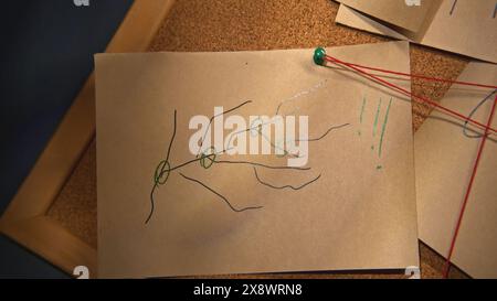 Planche avec notes et fils. Film de stock. Rébus sur des notes avec fil rouge. Gros plan d'images mystérieuses sur des notes avec fil rouge dans le bureau de nuit Banque D'Images
