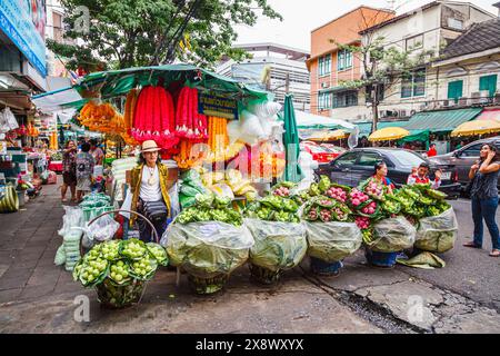 Stalle de bord de route et étallholder masculin vendant des fleurs colorées et des guirlandes à l'extérieur du marché aux fleurs en gros de Yodpiman Flower City à Bangkok, en Thaïlande Banque D'Images