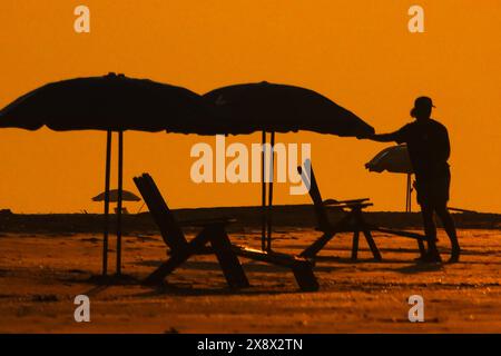 Île de Palms, États-Unis. 27 mai 2024. Un ouvrier, dessiné par le lever du soleil, dispose des parasols et des chaises en préparation pour les foules du Memorial Day, le 27 mai 2024 à Isle of Palms, Caroline du Sud. Crédit : Richard Ellis/Richard Ellis/Alamy Live News Banque D'Images