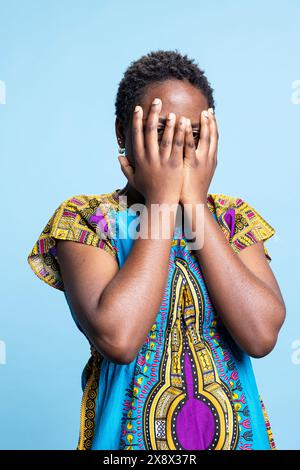 Femme d'ascendance afro-américaine ferme les yeux dans l'incrédulité et l'anxiété, hésitant à regarder quelque chose dans le studio. Jeune personne souffrant de nervosité intense et de panique, fille effrayée. Banque D'Images