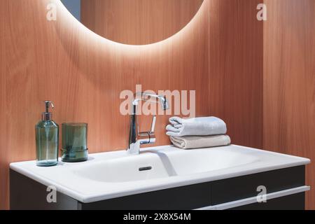 Un lavabo de salle de bain avec un robinet en argent et un lavabo blanc. Une bouteille verte et un vase vert sont sur le comptoir. Une serviette blanche est pliée et placée sur le Banque D'Images