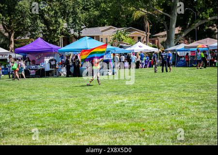 Roseville, CA, États-Unis - 18 mai 2024 : une personne non identifiée porte un drapeau arc-en-ciel devant des stands sur la zone herbeuse de Royer Park pendant placer Pride. Banque D'Images