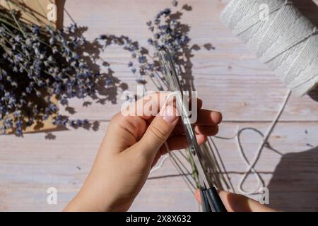 Femme créant des bouquets de fleurs de lavande sèches. Procédé de fabrication de bouquets parfumés et de sachets à partir d'herbes cultivées à domicile. Médecine alternative étape par étape. BRICOLAGE Banque D'Images