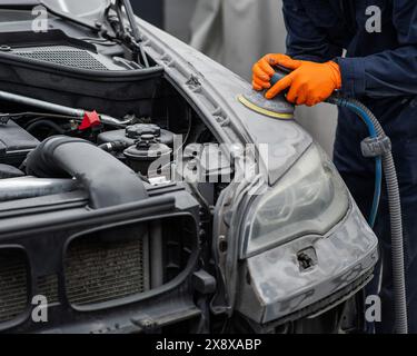 Un mécanicien ponce le mastic sur une carrosserie de voiture avec une machine. Réparation après un accident. Banque D'Images