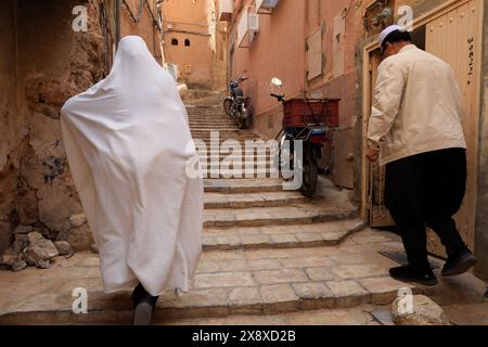 Une femme mozabite en haik blanc marchant dans la rue étroite de Ksar Ghardaia avec un homme à côté. Vallée de Mzab. Province de Ghardaia. Sahara du Nord. Algera Banque D'Images