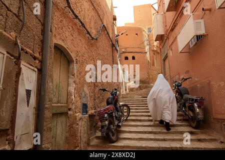 Une femme mozabite en haik blanc marchant dans la rue étroite de Ksar Ghardaia. Ghardaïa est l'un des ksar (colonie fortifiée) dans la vallée du Mzab. Province de Ghardaia. Sahara du Nord. Algérie Banque D'Images