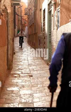 Un jeune garçon faisant du vélo dans une rue de pierre rétrécie à l'intérieur de Ksar El Atteuf. Vallée de Mzab. Province de Ghardaia. Sahara du Nord. Algérie Banque D'Images