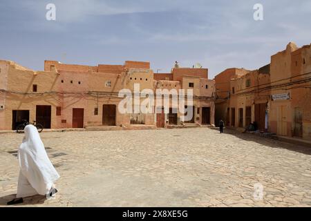 Une femme mozabite voilée en haik blanc sur la place du marché de Beni Isguen avec des architectures mozabites traditionnelles en arrière-plan. Beni Isguen est l'un des 5 Ksars (colonie fortifiée) de la vallée du Mzab. Province de Ghardaia. Sahara du Nord. Algérie Banque D'Images