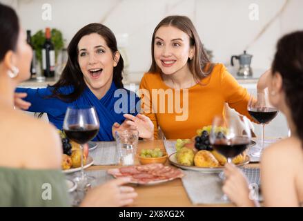 Des femmes heureuses se sont rassemblées autour d'une table festive ; participant à des discussions animées et appréciant les délices du vin Banque D'Images