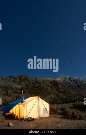 Tente chaude dans le camp de chasse incandescent sous le ciel étoilé de nuit, Thomas Creek, Frank Church River of No Return Wilderness, Idaho, États-Unis Banque D'Images