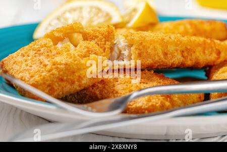 gros plan de filet de pollock d'alaska croustillant cuit au four sur un plat bleu avec des tranches de citron sur une table en bois blanc Banque D'Images