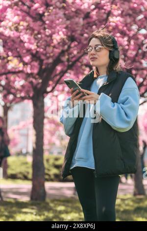 femme mélomane vérifiant des chansons sur son téléphone copie espace florissant sakura sur fond Banque D'Images