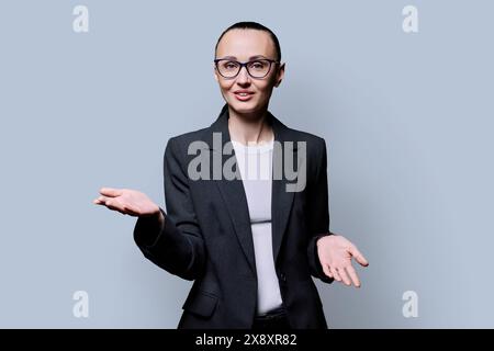 Parler femme d'âge moyen d'affaires regardant la caméra sur fond gris de studio Banque D'Images