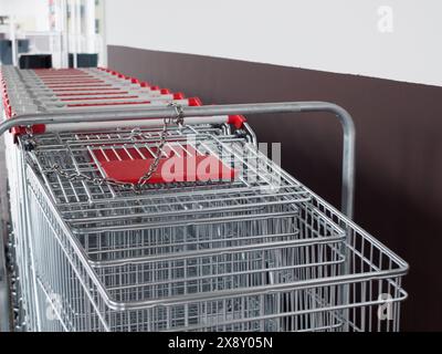 Rangée de chariots métalliques avec poignées rouges soigneusement disposés à l'intérieur d'une épicerie moderne avec une ambiance lumineuse et aérée Banque D'Images