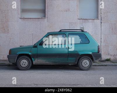 Cremona, Italie - 15 mai 2024 Vieux turquoise Fiat Panda rétro mini fourgonnette se trouve abandonné par un bâtiment aux murs altérés, illustrant urb Banque D'Images