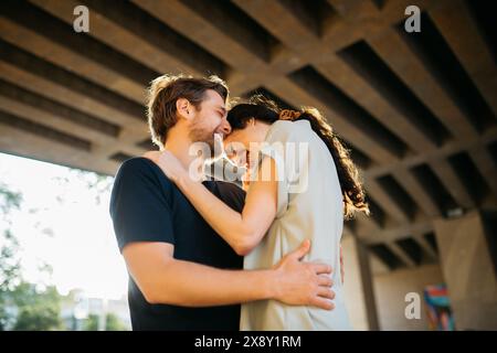 Couple partageant une étreinte joyeuse et tendre, souriant et se penchant les uns dans les autres sous un plafond structuré avec la lumière du soleil filtrant à travers le backgro Banque D'Images