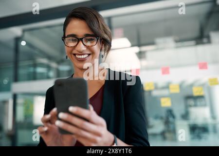 Téléphone, sourire et femme d'affaires dans le bureau en tapant un e-mail ou réseautage sur Internet. Communication, technologie et concepteur professionnel faire Banque D'Images