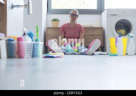 Femme ennuyée frustrée assise sur le sol dans la salle de bain, elle nettoie sa maison Banque D'Images