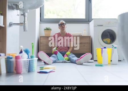 Femme ennuyée frustrée assise sur le sol dans la salle de bain, elle nettoie sa maison Banque D'Images