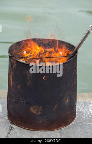 Le bois de chauffage brûle dans un tonneau de fer. Gros plan incendie. Brûler les déchets de jardin dans un vieux tonneau de fer. Les langues de flamme montent vers le haut. un feu brûle dans un iro Banque D'Images