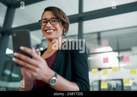 Smartphone, sourire et femme d'affaires professionnelle dans le bureau en tapant un e-mail ou en réseautant sur Internet. Communication, technologie et design Banque D'Images