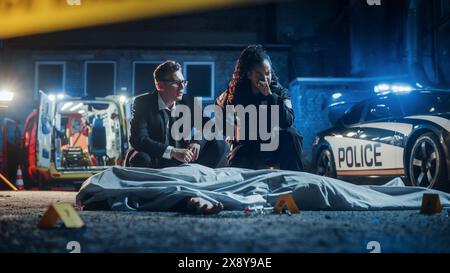 Portrait de deux policiers travaillant sur une affaire la nuit en visitant une scène de crime dans une allée arrière. Détective masculin et une Policewoman considérant des indices et des preuves pour résoudre un meurtre brutal Banque D'Images