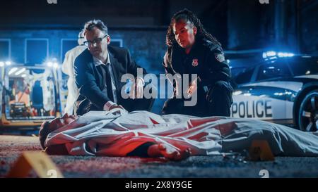 Policiers arrivant à la scène du crime la nuit. Détectives retirez la couverture du visage de la victime pour l'identifier et vérifier l'état du cadavre. Jeune homme mourant dans un accident de la circulation avec excès de vitesse Banque D'Images