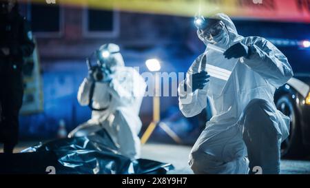 Portrait de deux experts en médecine légale qui font du travail sur le terrain la nuit sur une scène de crime. Un technicien prend des photos du cadavre tandis que l'autre emballe le couteau ensanglanté comme arme du crime. Banque D'Images