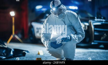 Portrait de deux experts en médecine légale qui font du travail sur le terrain la nuit sur une scène de crime. Un technicien emballe le couteau ensanglanté comme arme du crime tandis que l'autre prend des photos du cadavre. Banque D'Images