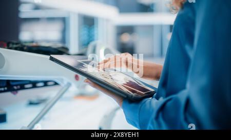 Gros plan d'une femme utilisant un ordinateur tablette dans un bureau industriel moderne de haute technologie. Ingénieur programmation et configuration d'un concept de robot moderne sur un appareil intelligent. Banque D'Images