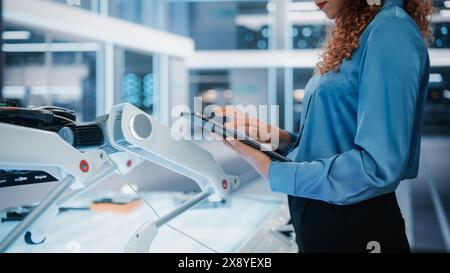 Gros plan d'une femme utilisant un ordinateur tablette dans un bureau industriel moderne de haute technologie. Ingénieur programmation et configuration d'un concept de robot moderne sur un appareil intelligent. Banque D'Images