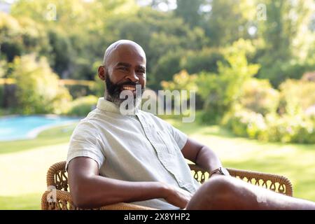 Un homme aîné afro-américain, portant des vêtements légers, assis dehors, souriant Banque D'Images