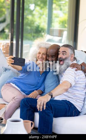 Divers amis seniors prenant selfie joyeux canapé à la maison Banque D'Images