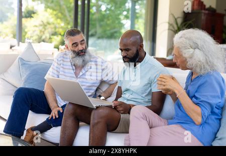Divers amis seniors se réunissant autour d'un ordinateur portable à la maison Banque D'Images
